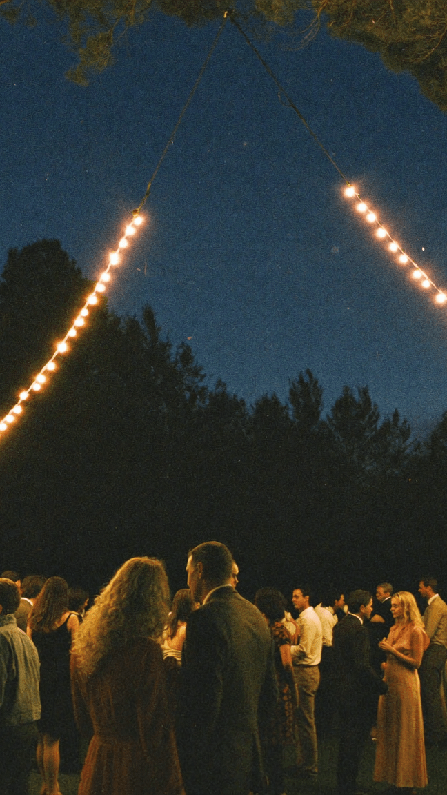 Wedding guests dancing at night under string lights strung through pine trees